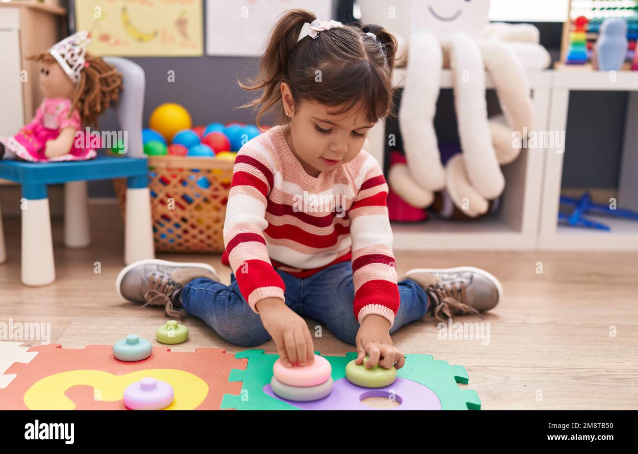 Adorable hispanic girl playing with toys sitting on floor at ...