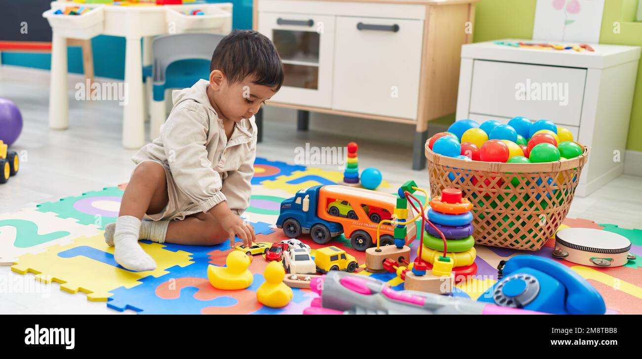 Adorable hispanic toddler playing with car toy sitting on floor at ...