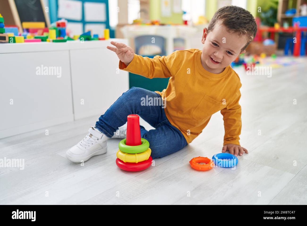 Adorable caucasian boy playing with hoops toy sitting on floor at ...