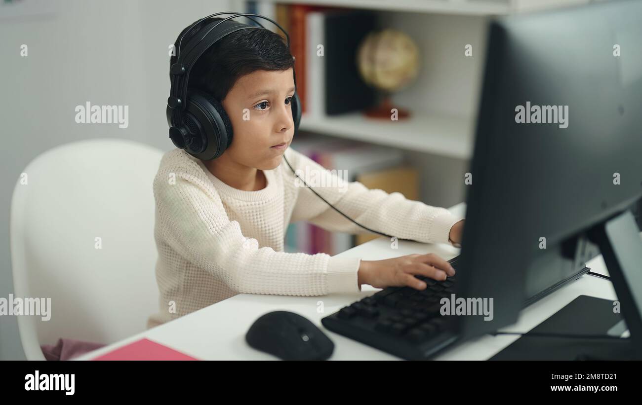 Adorable hispanic boy student using computer sitting on table at ...