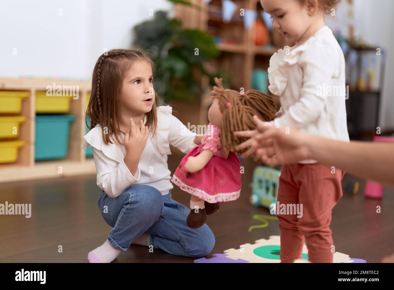 Two little girls playing with dolls sitting on floor at kindergarten ...