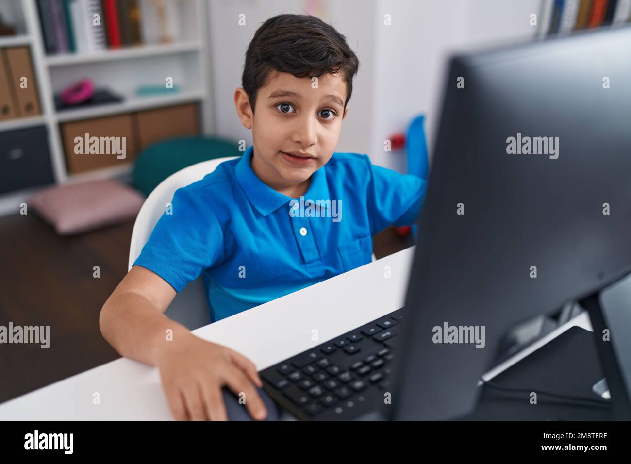 Adorable hispanic boy student using computer sitting on table at ...
