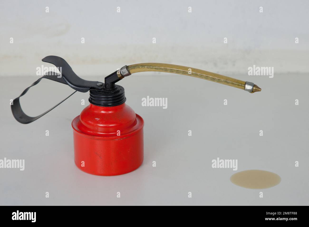 oil stain. A red oil can with a flexible spout stands on the white workbench. From his tip Oil dripped onto the work surface. Stock Photo