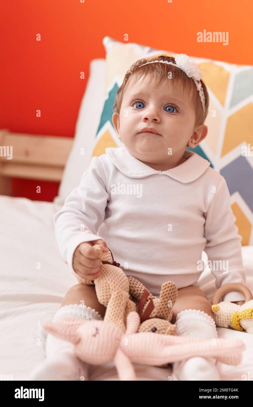 Adorable blonde baby holding toy sitting on bed at bedroom Stock Photo ...