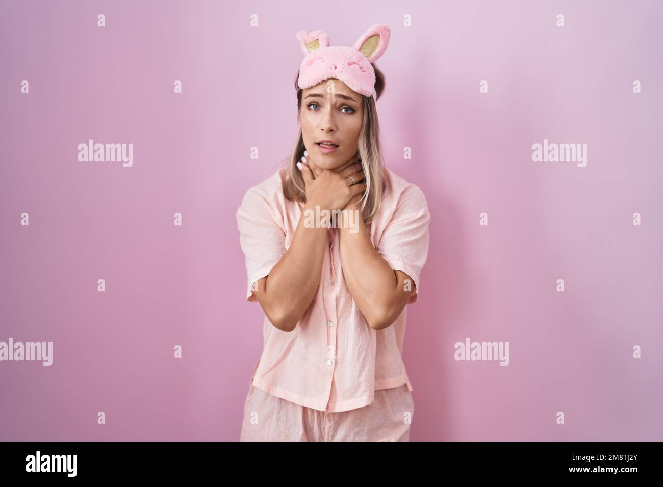 Blonde caucasian woman wearing sleep mask and pajama shouting suffocate