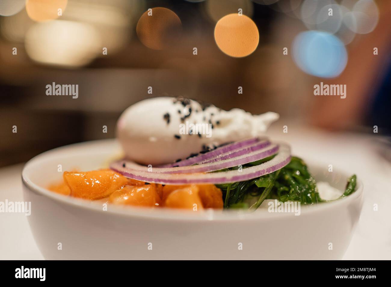 Selective focus Asian salmon poke bowl with blurred background party night lights, Stock Photo