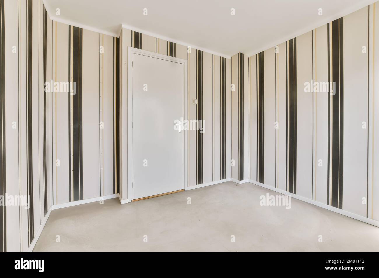 an empty room with black and white striped wallpapers on the walls there is a door in the corner Stock Photo