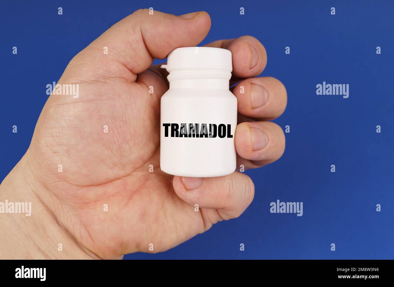 Pharmacology concept. On a blue background in the hands of a man is a white jar with the inscription - Tramadol Stock Photo