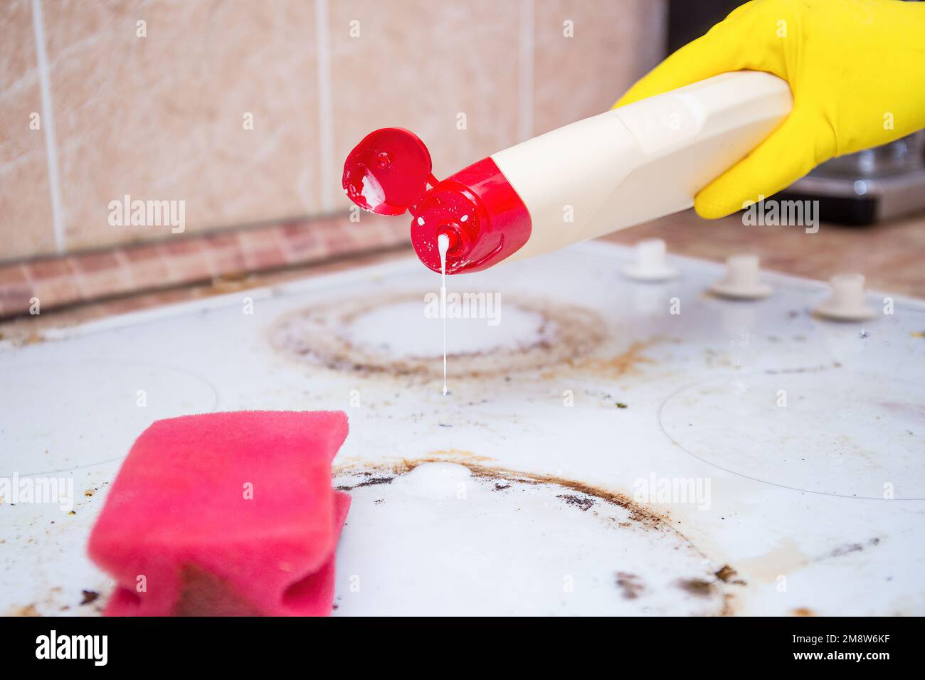 Man cleaning ceramic modern stove or hob with detergent agent. Hand in yellow gloves clean stove