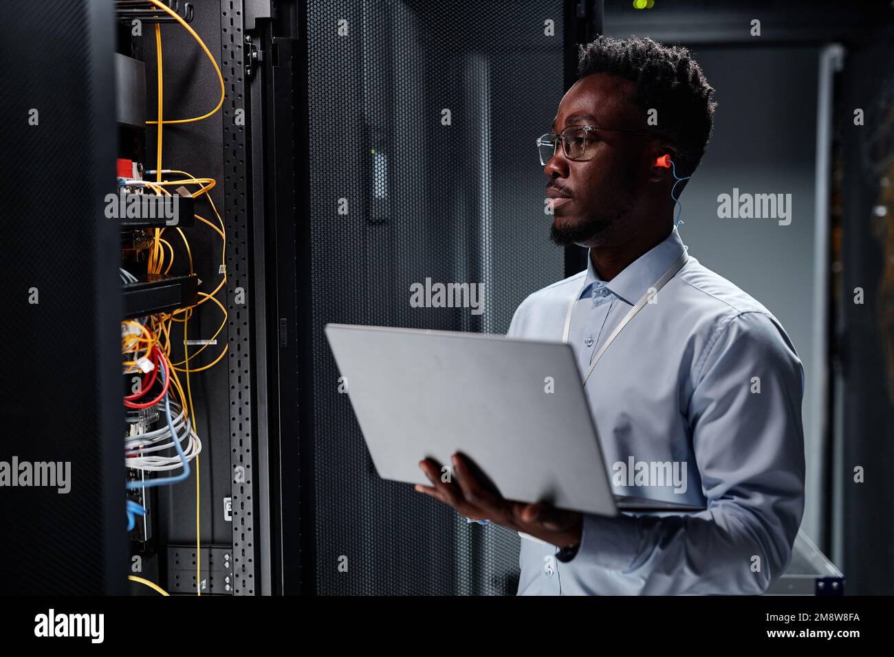 Waist up portrait of black man as network engineer in server room using laptop, minimal Stock Photo