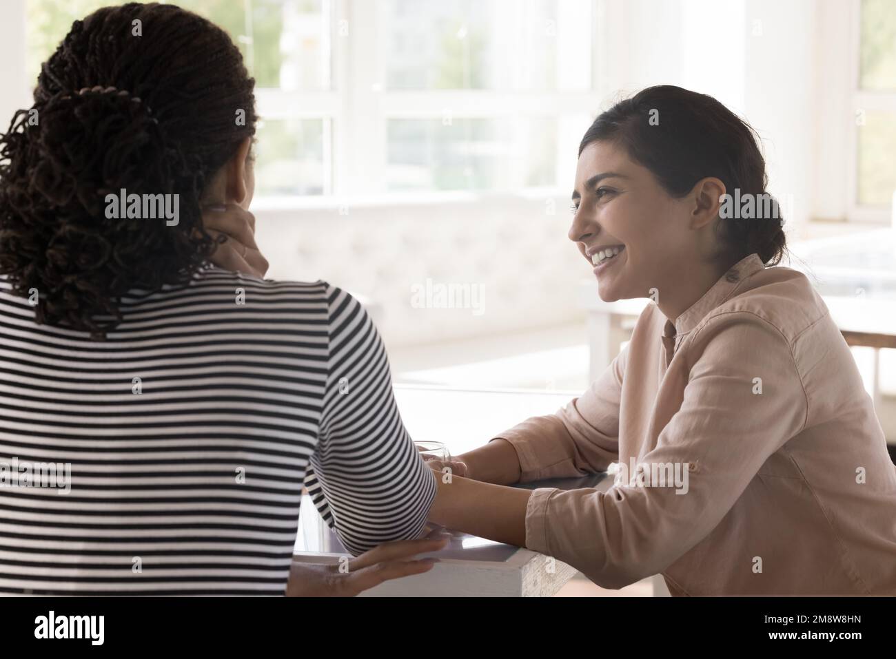 Happy Indian woman and African female friend sitting at table Stock Photo