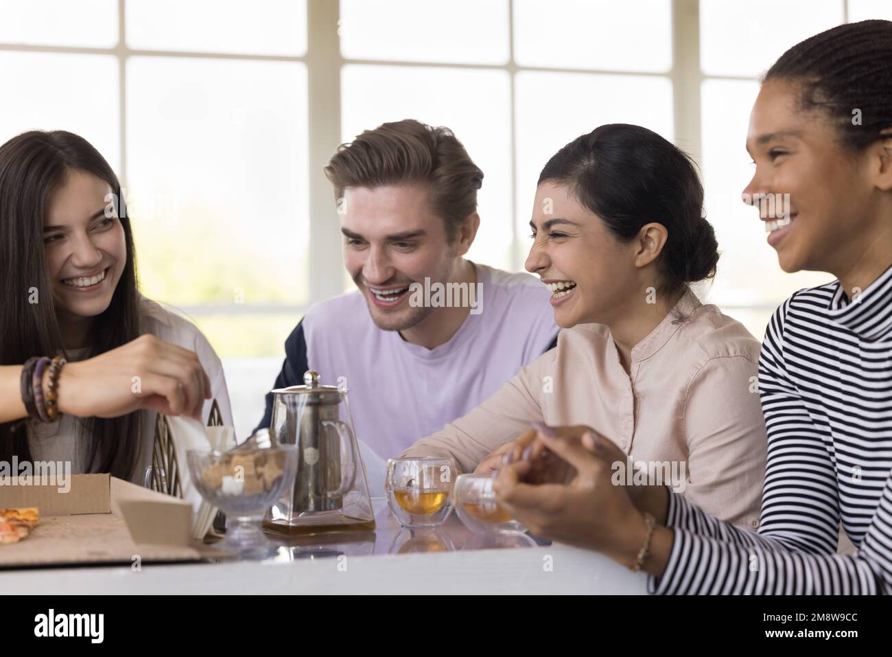 Diverse group of young friends gathering at table in cafe Stock Photo