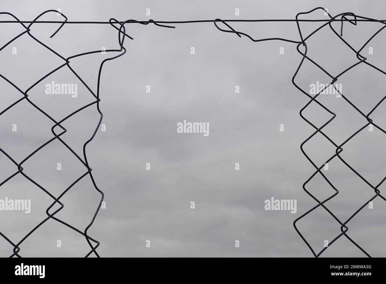 Chain link fence hole damage wire shapes and cloudy sky background. Stock Photo