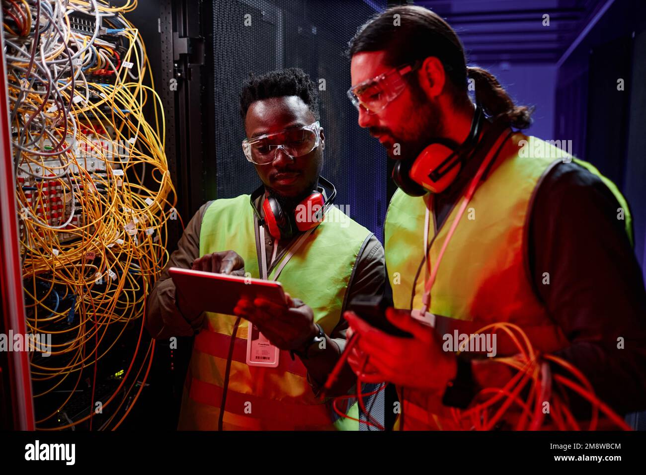 Close up of two network technicians using tablet while repairing server in neon light Stock Photo