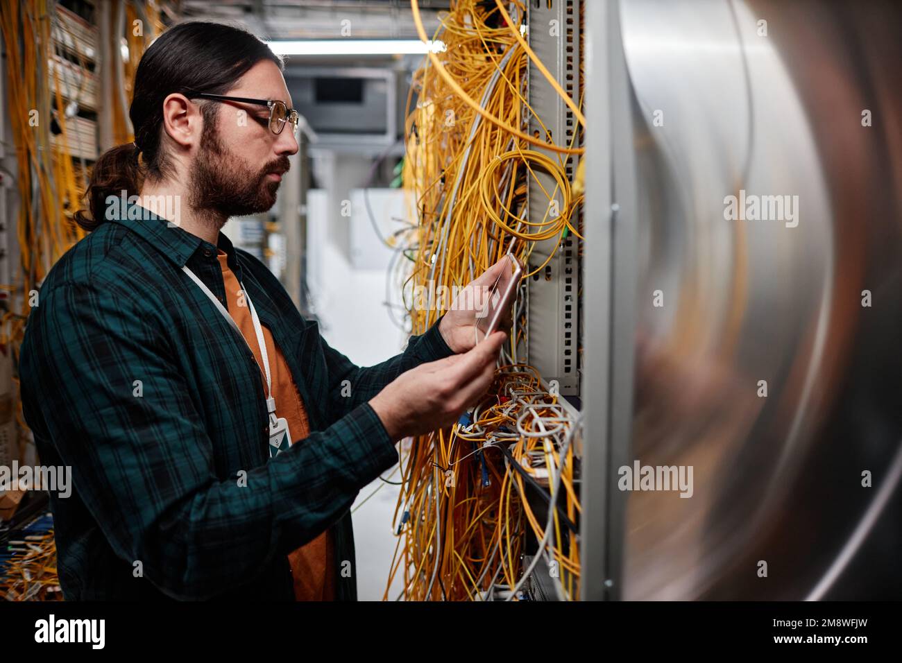 Side view portrait of bearded system administrator setting up server and using smartphone Stock Photo