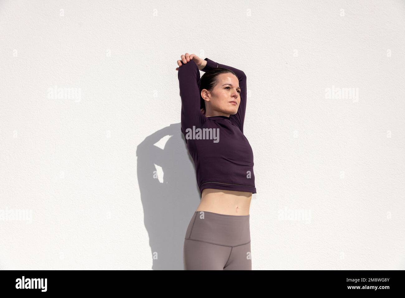 fit sporty woman doing an arm stretch warm up exercise outside against a white wall Stock Photo