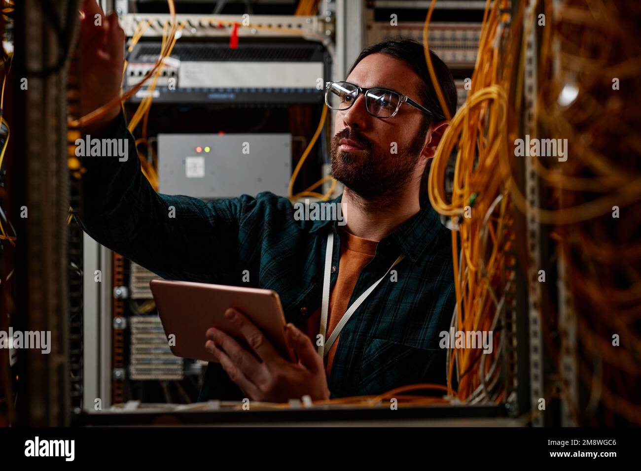 Front view portrait of bearded man setting up server while working with data network and holding tablet Stock Photo