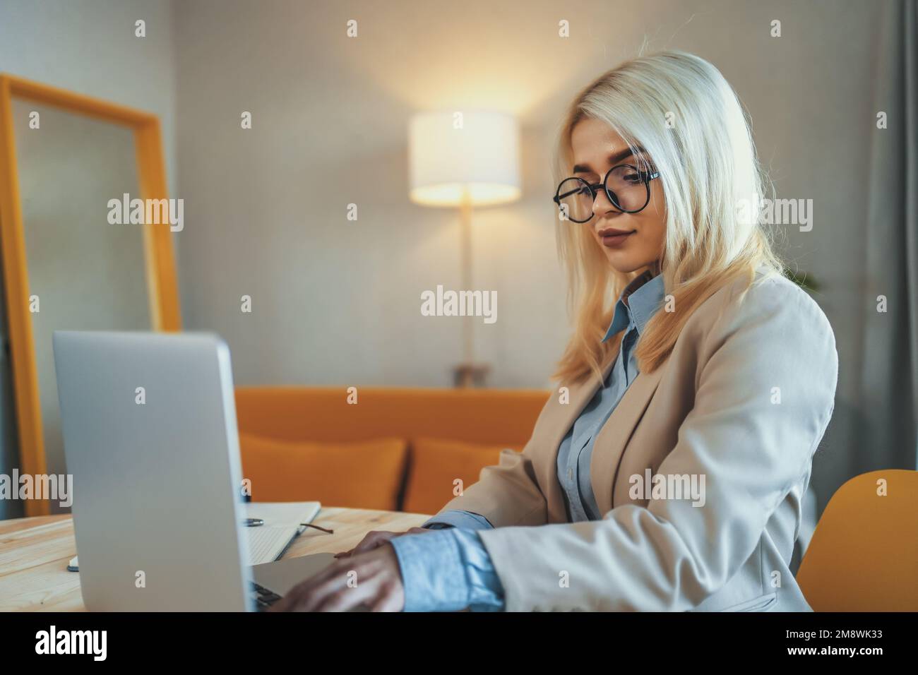 Young beautiful blonde businesswoman or college student works on laptop at home or in office. Online seminar, distance learning or job concept. Stock Photo