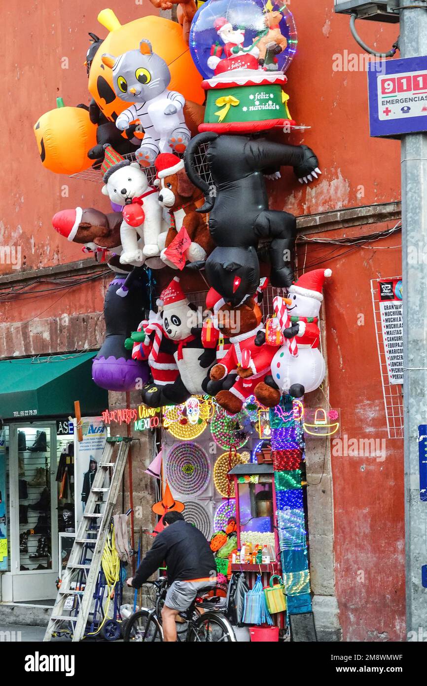 A stack of inflatable characters decorates a shop selling novelty items on Moneda Street with the dome of the Templo de Santa Inés church in the Zona Centro neighborhood of Mexico City, Mexico. Stock Photo