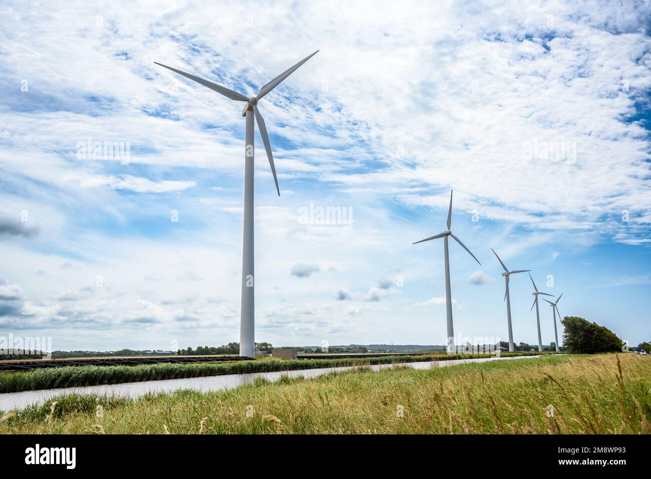 Wind turbines and solar panels on the bank of a canal in the countryside on a partly cloudy summer day Stock Photo