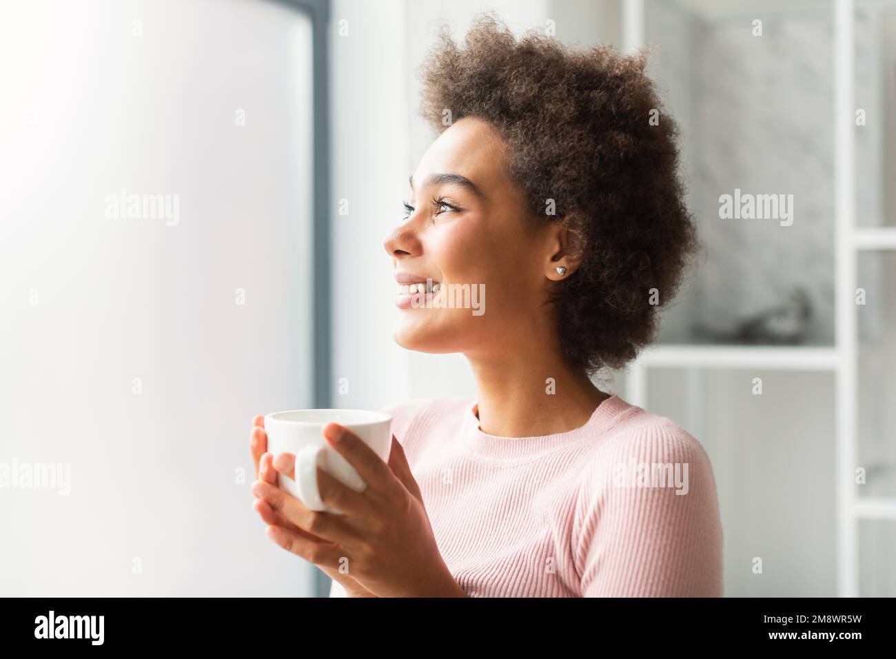 Cheerful pretty millennial mixed race female looking at empty space, dreaming, holding coffee cup alone Stock Photo