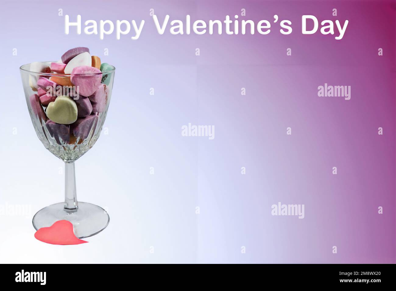 Crystal wine glass holding Valentine heart candy isolated on gradient white to violet background with words Happy Valentines Day - Just add text - roo Stock Photo