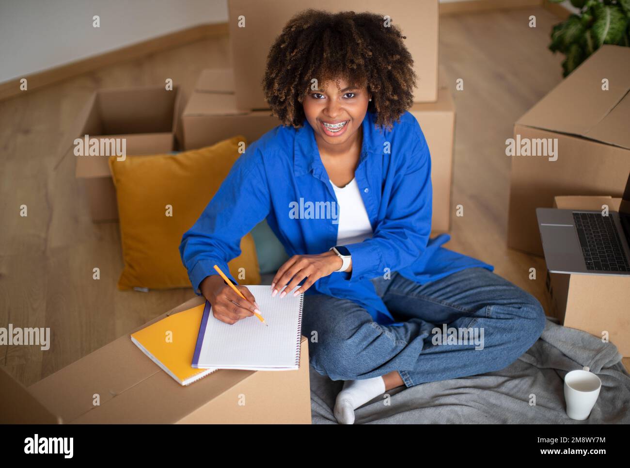 Black Woman Sitting Among Cardboard Boxes After Moving And Writing In ...