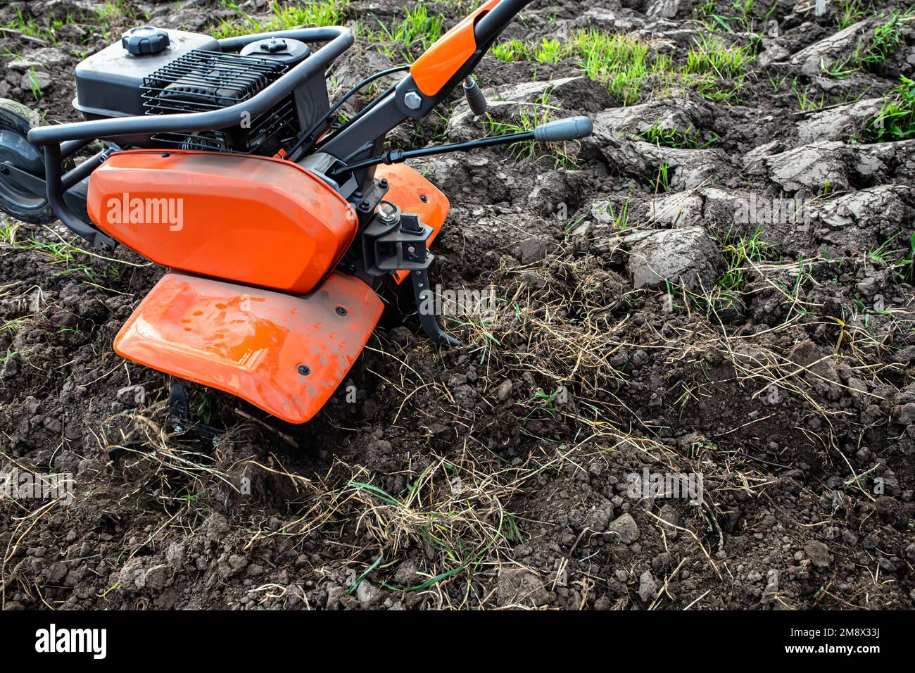Orange professional cultivator or tiller on untreated soil before