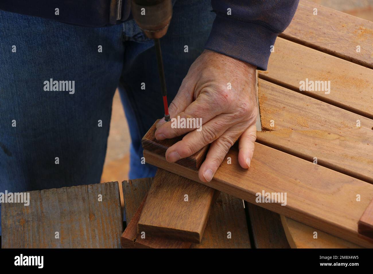 Close up of the hands of a senior man who is using a drill bit to complete a woodworking project to build flooring. Stock Photo