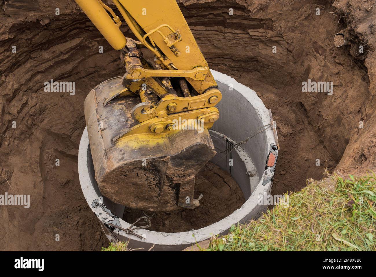 Excavator with a bucket, lowering into the pit on steel cables concrete ...