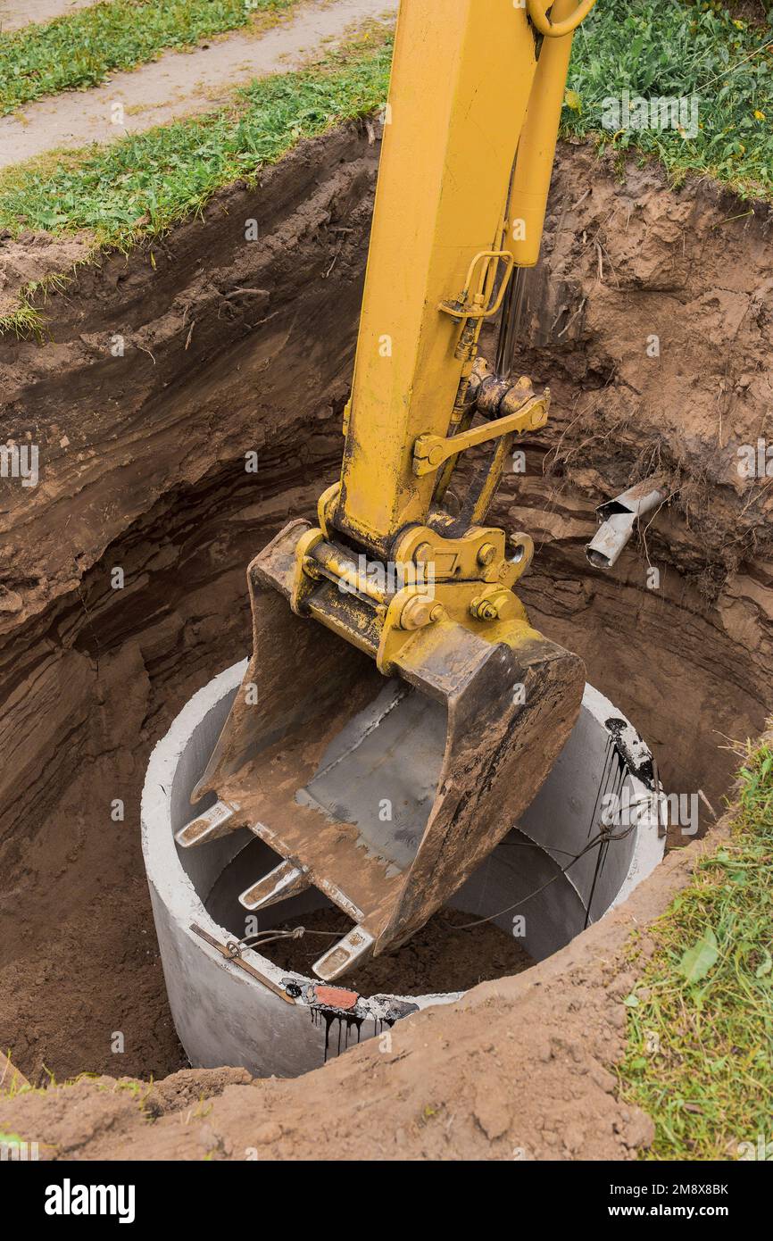 Excavator with a bucket, lowering into the pit on steel cables concrete ...