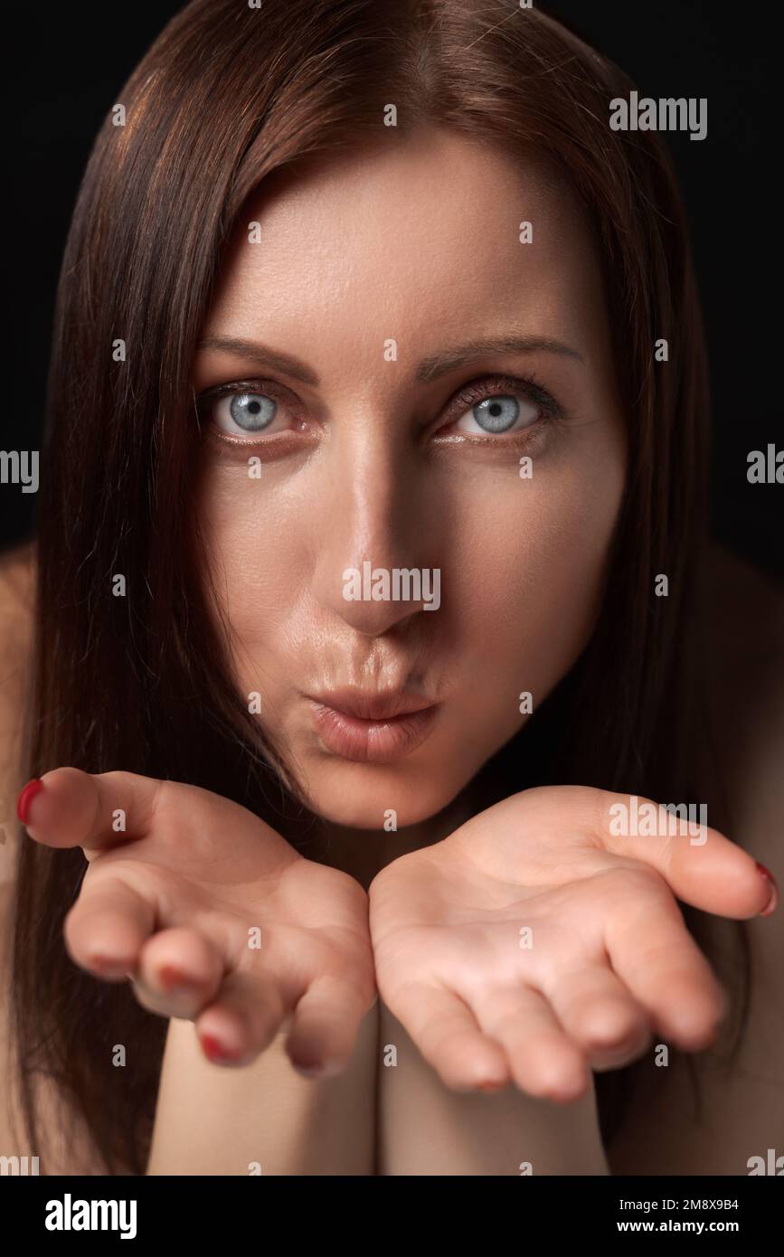 Adult woman blowing lips send air kiss over palms to her boyfriend and looking at camera. 40-year-old woman with gray eyes demonstrates good feelings Stock Photo