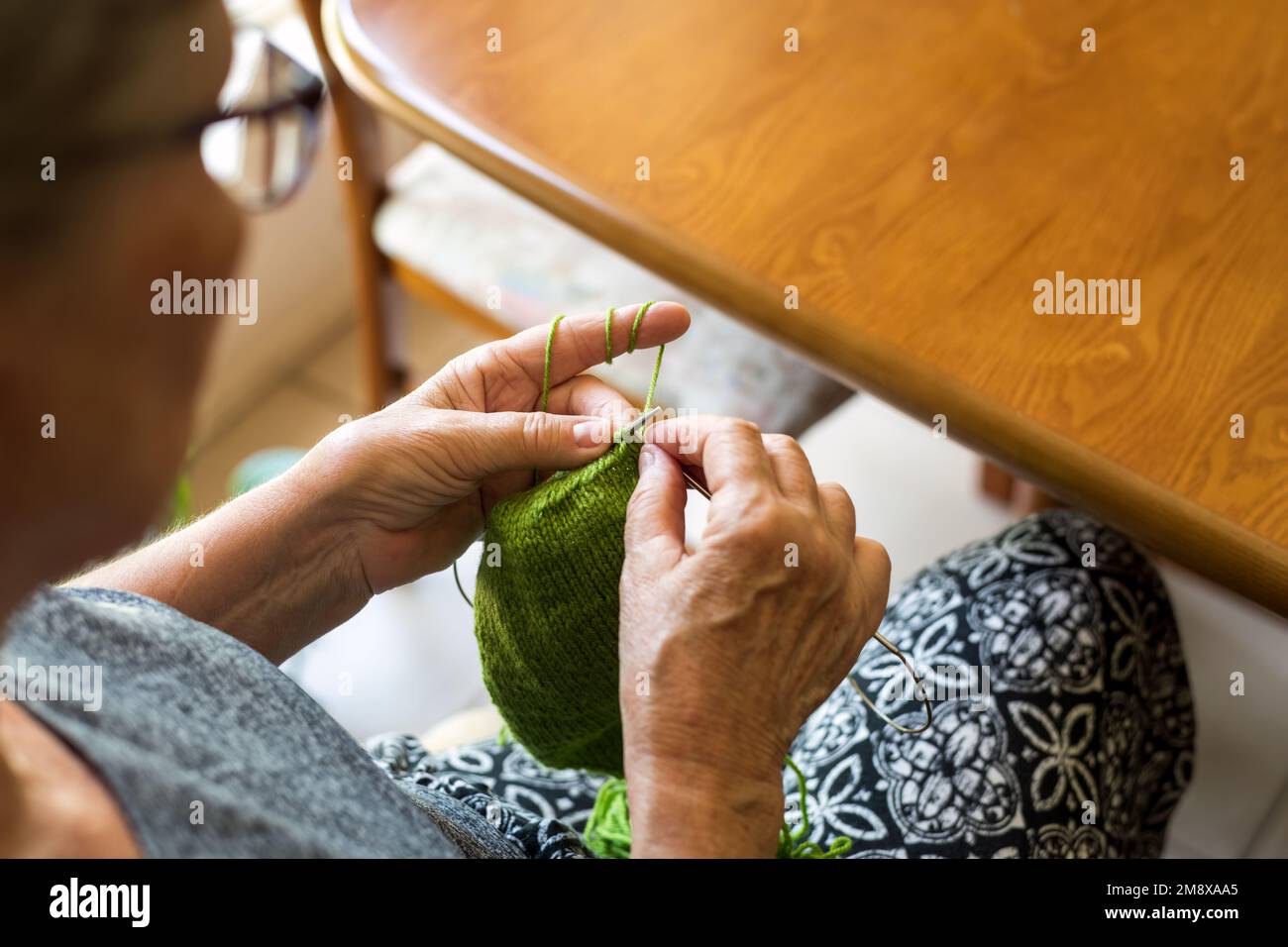 Close-up of hands of an older woman knitting socks with green wool and ...