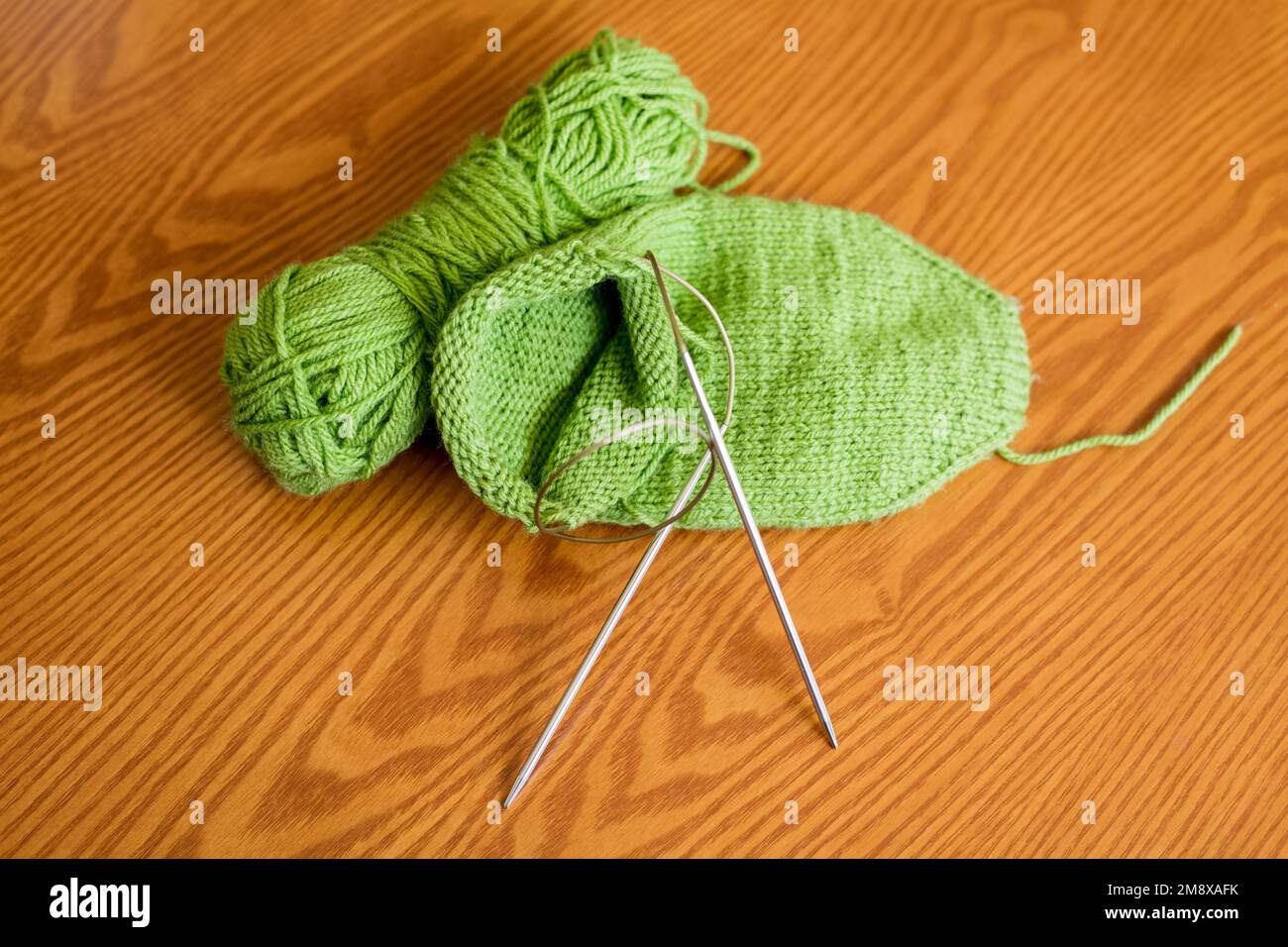 Knitted sock, ball of yarn and circular knitting needles on a wooden table surface. Top view. Stock Photo