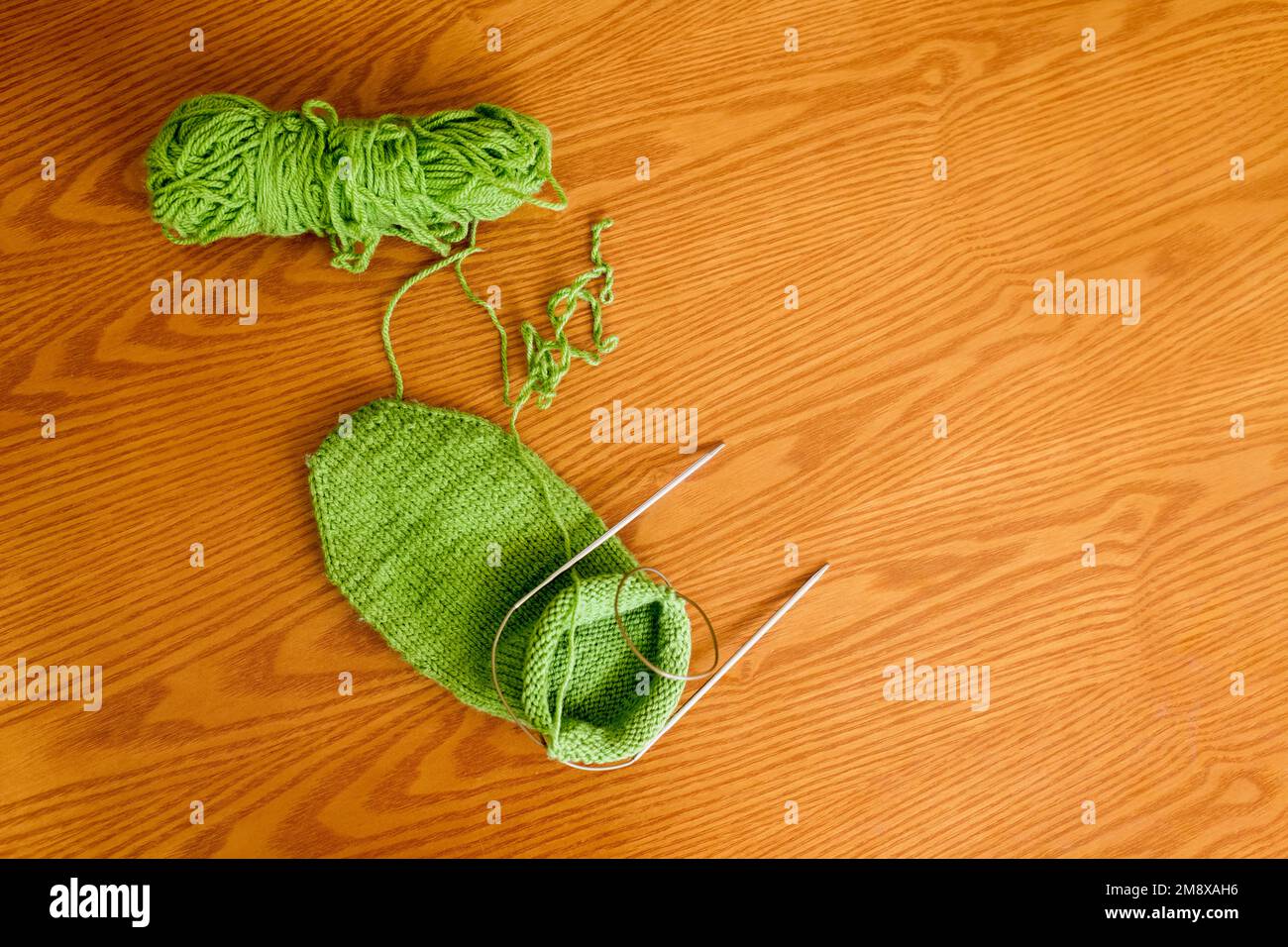 Knitted sock, ball of yarn and circular knitting needles on a wooden table surface. Top view with copy space. Stock Photo