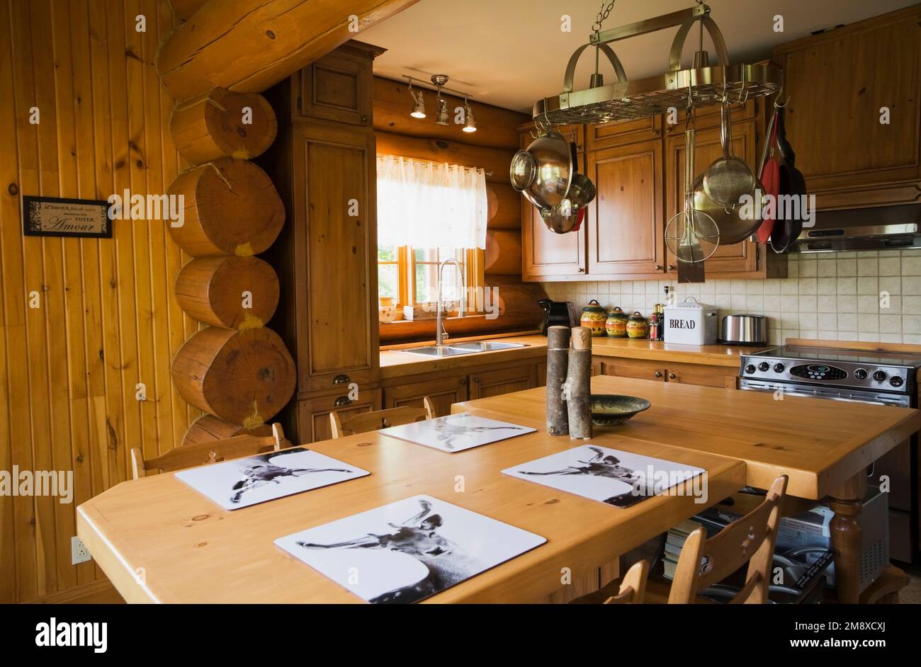 Pine wood cabinets, dining table and island in kitchen inside Scandinavian cottage style log home. Stock Photo