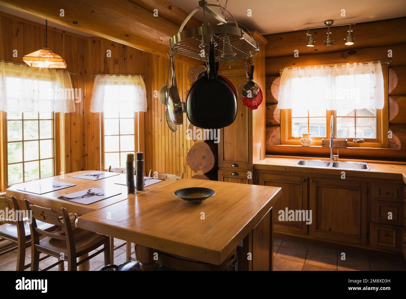 Pine wood cabinets, dining table and island in kitchen inside Scandinavian cottage style log home. Stock Photo