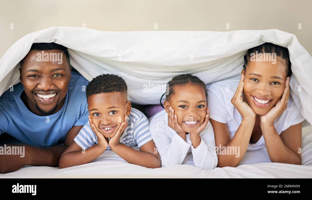 Our little ones keep us young. a young family bonding together while lying on the bed at home and under the duvet. Stock Photo
