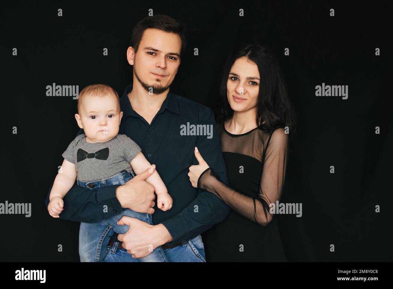 Happy white Caucasian family on black background. Mom and dad with baby infant boy in hands Stock Photo