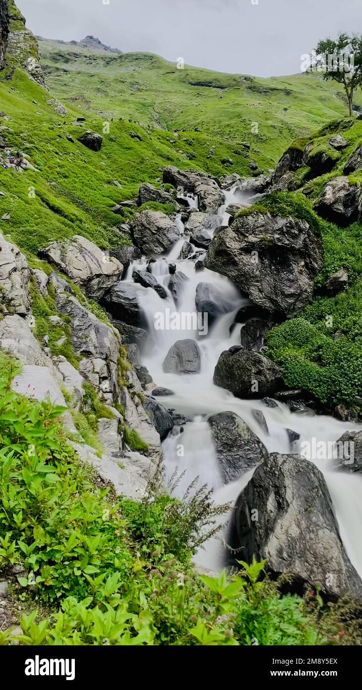 A vertical shot of a river flowing through the green hills of Hampta ...