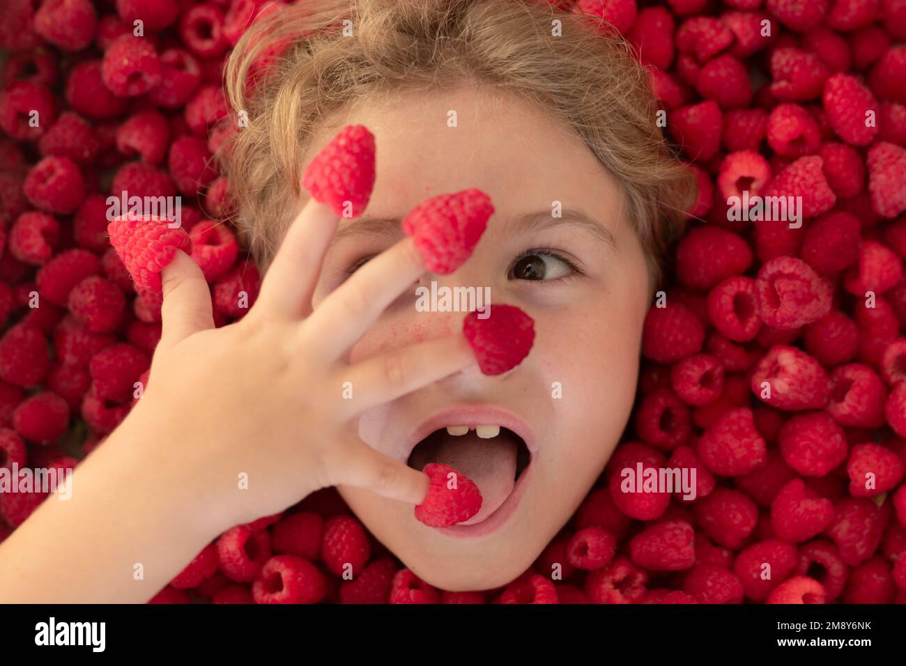 Kid Raspberry Fresh raw raspberry near kids face. Raspberri macro. Top view of ...