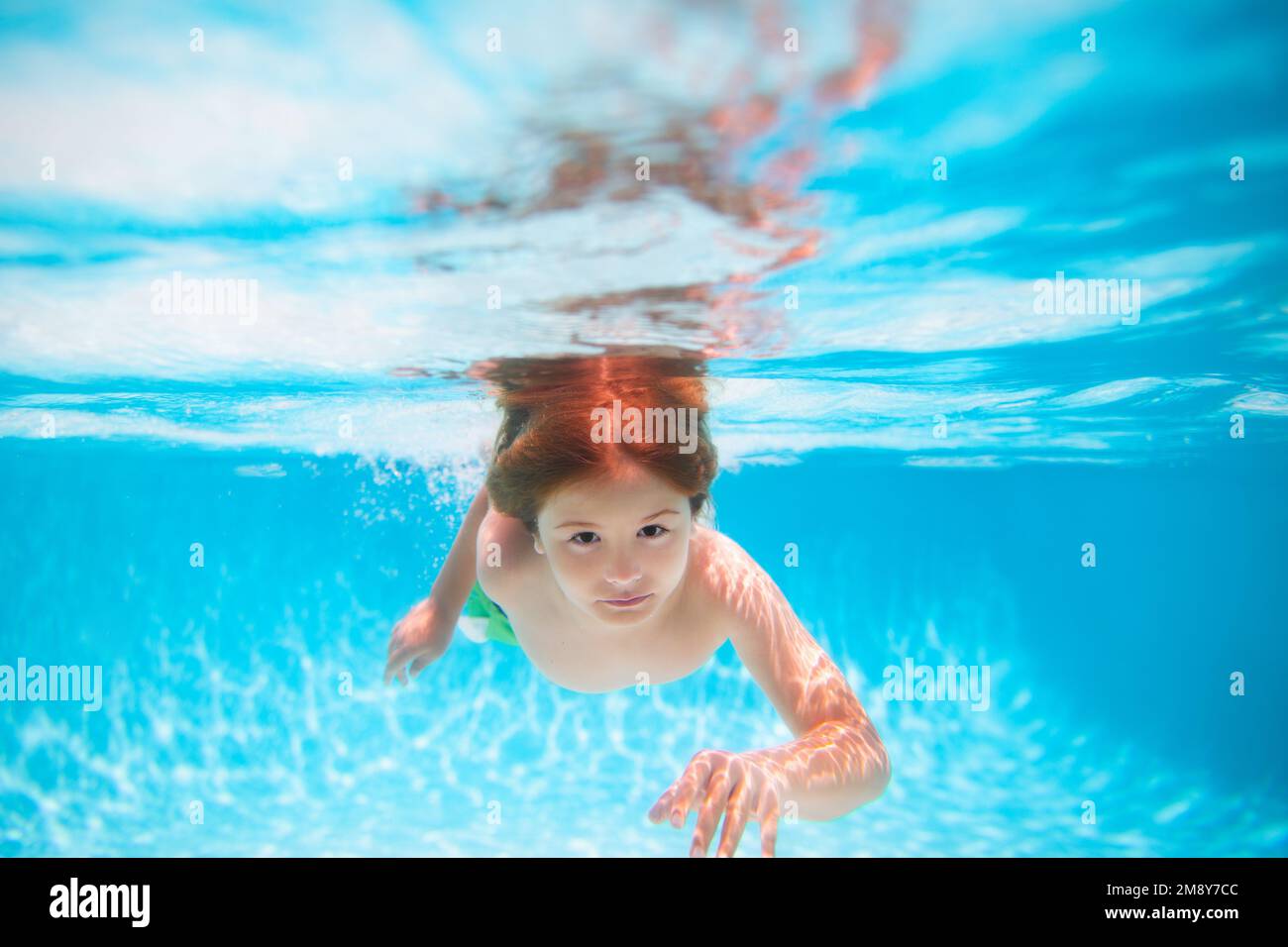 Child swimming underwater in swimming pool. Funny kids boy play and