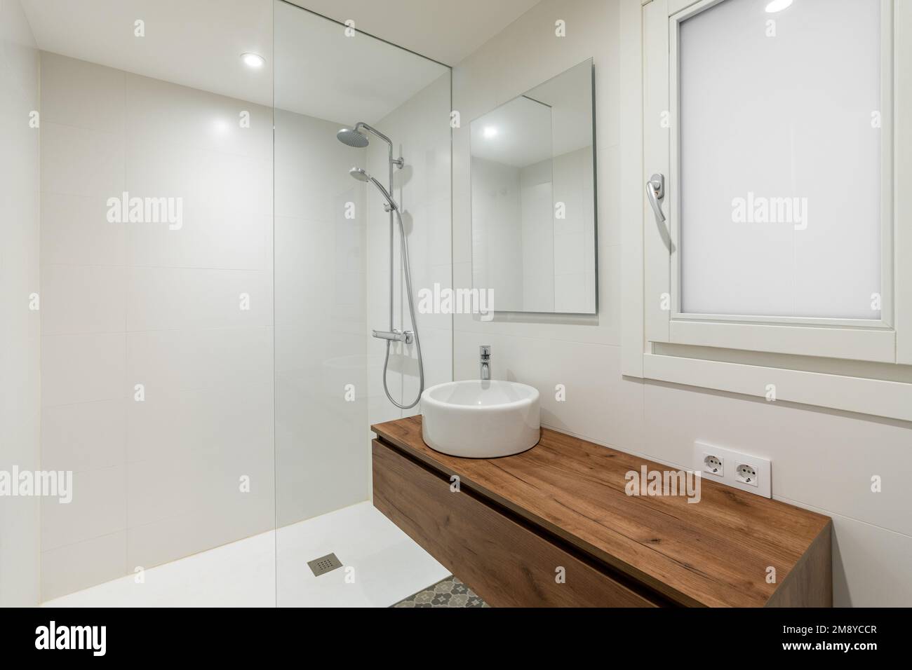 Bathroom with small round white sink on long wooden countertop floating in air. Mirror above