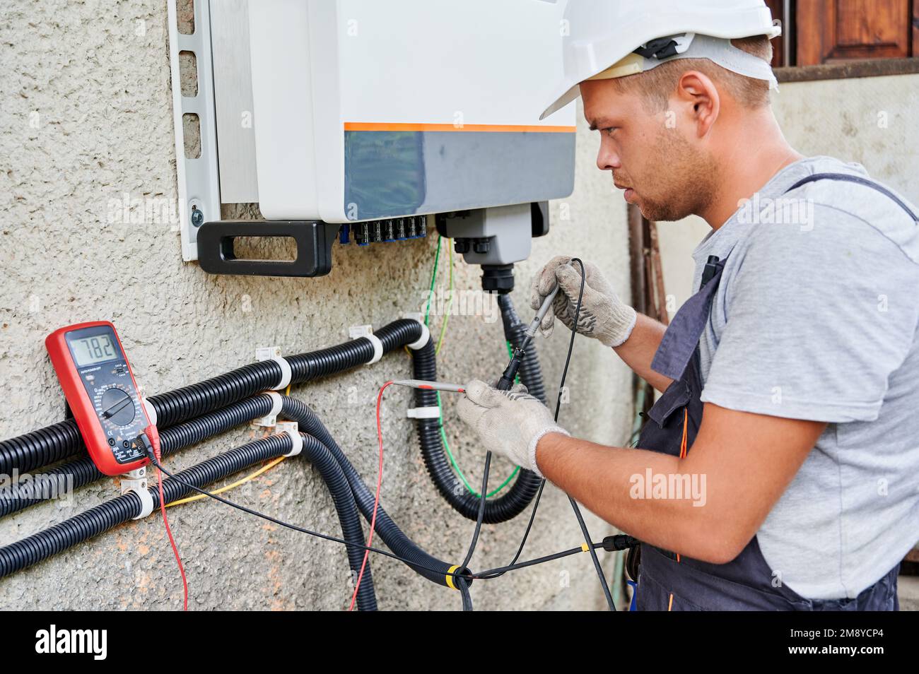 Man electrician installing solar panel system. Inspector in helmet and gloves making electrical wiring inverter and electric box. Concept of alternative and renewable energy. Stock Photo