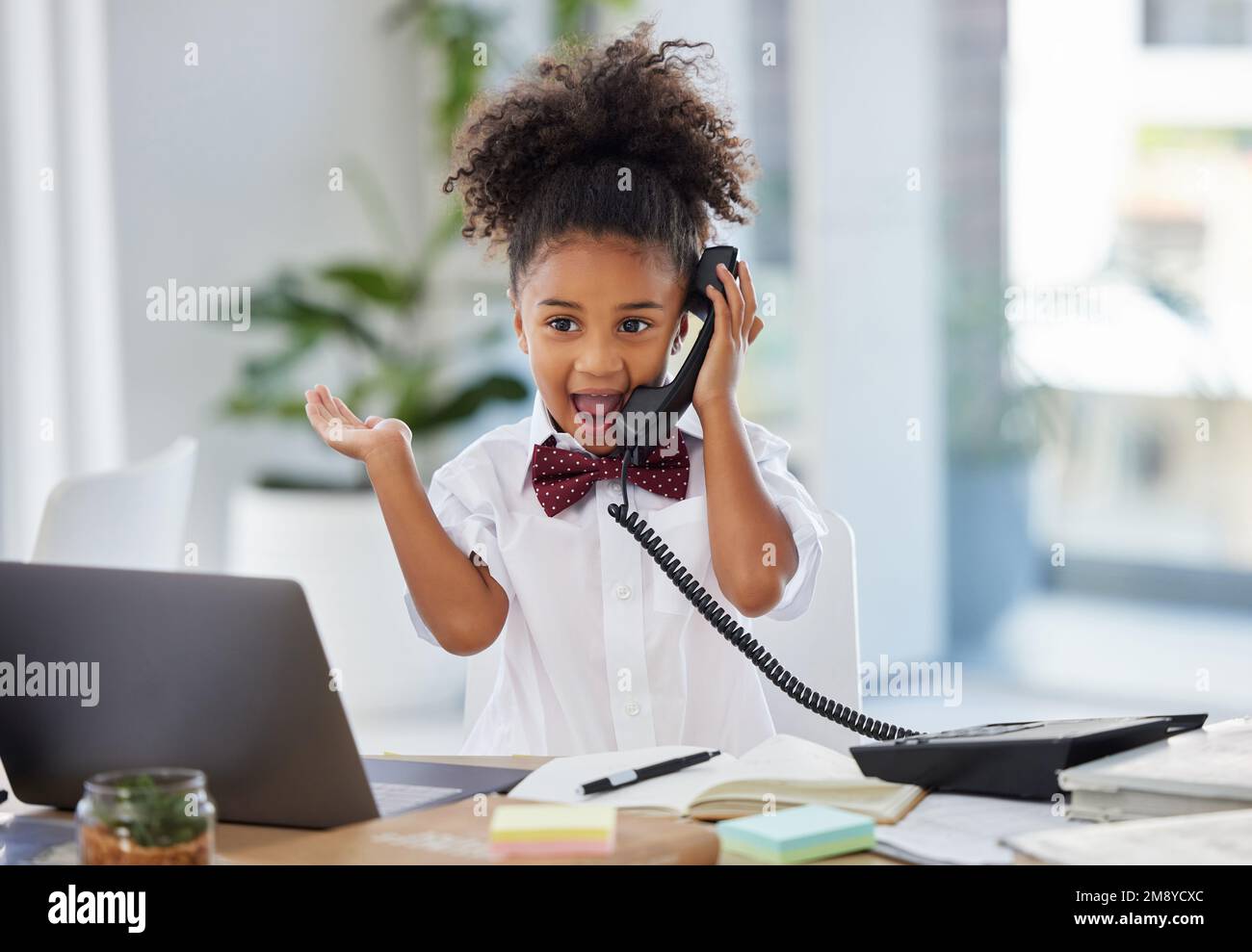 Yay. an adorable little girl dressed as a businessperson sitting and looking surprised while using a telephone. Stock Photo