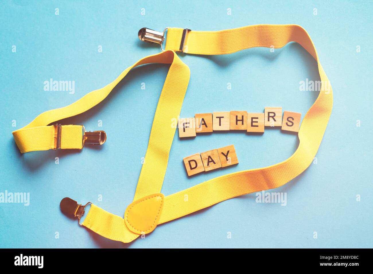 happy father's day lettering made by wooden cubes on a blue background with a yellow suspenders. Stock Photo