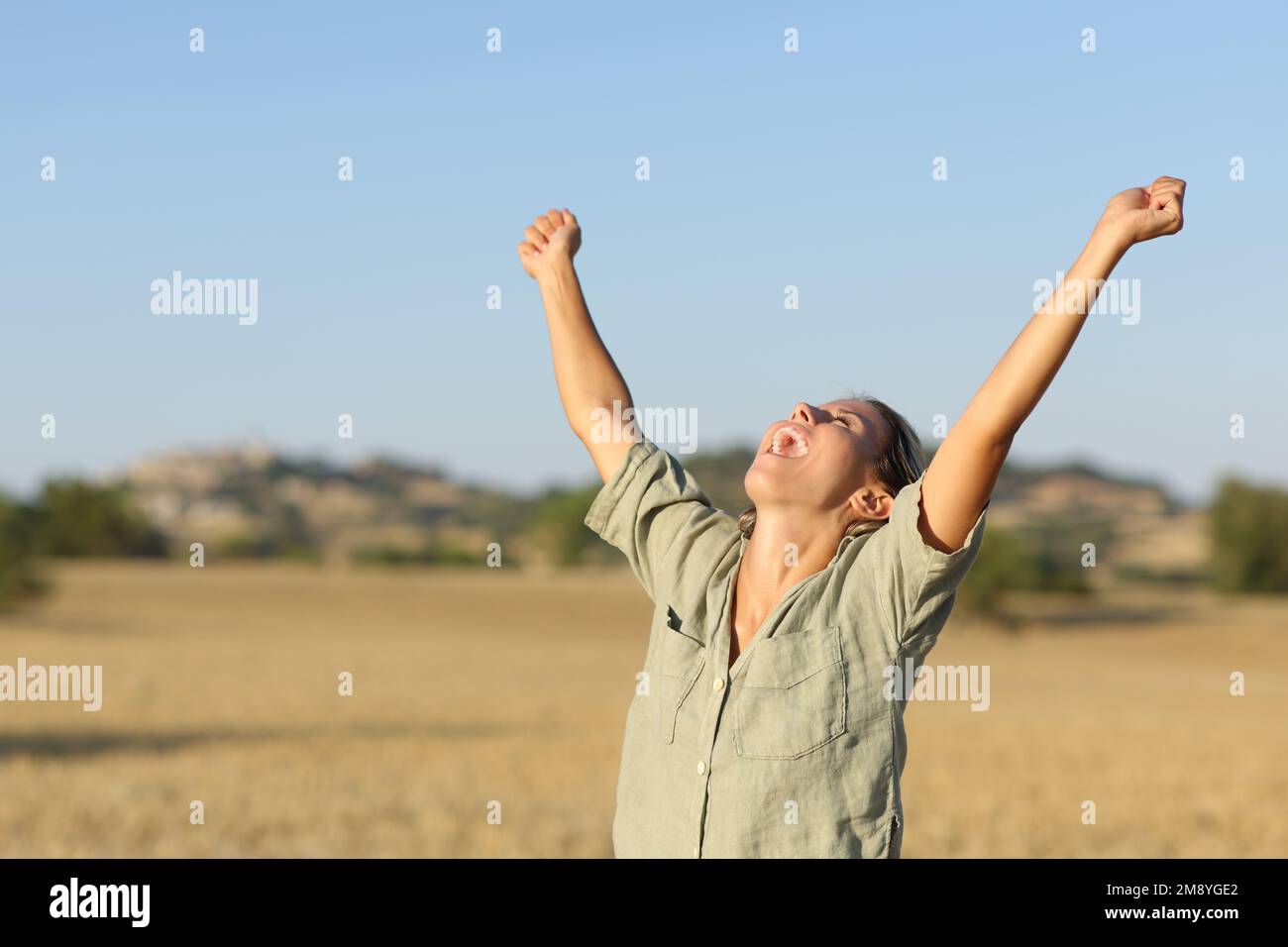 Excited woman raising arms in a field on summer Stock Photo