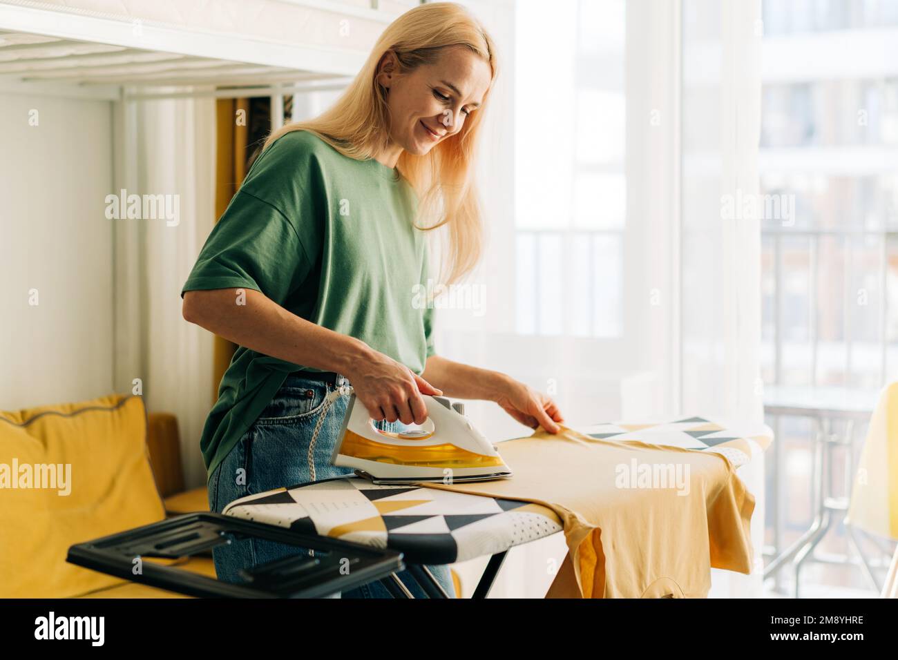 Middle-aged woman housewife ironing clothes at home. Stock Photo