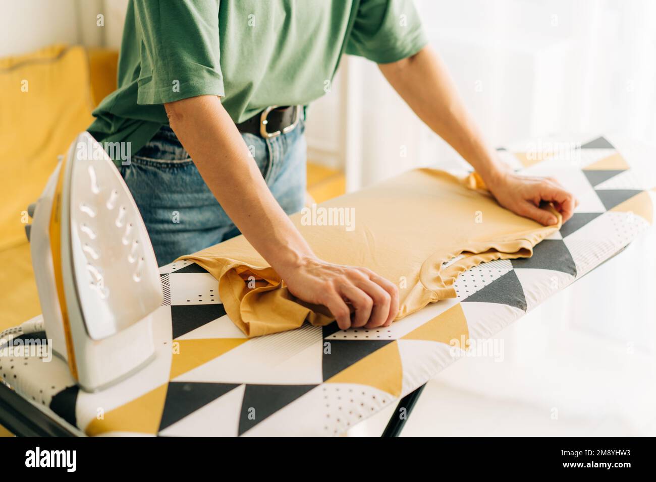 Close-up of an unrecognizable woman ironing linen on an ironing board. Stock Photo
