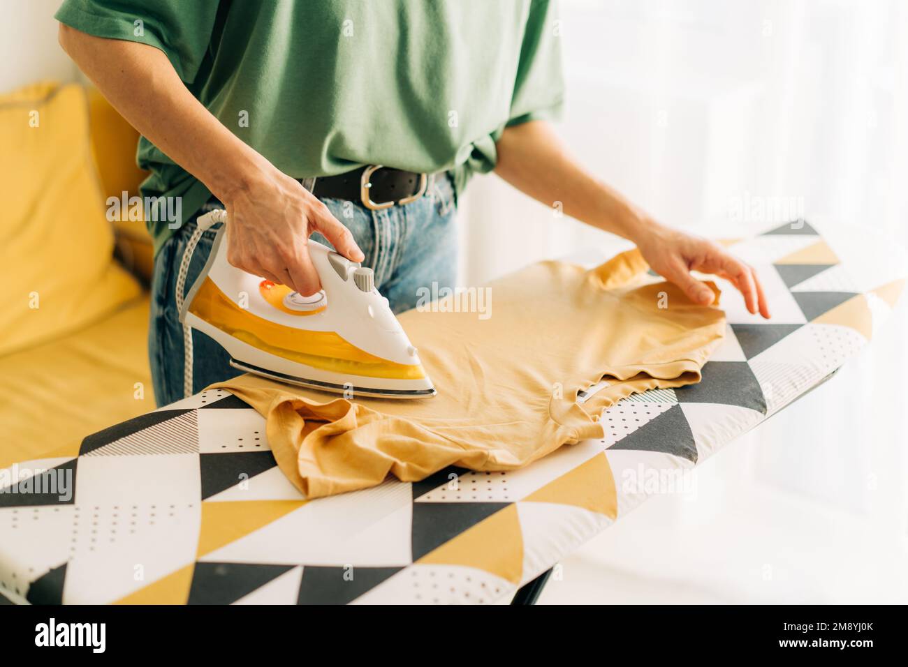 Close-up of an unrecognizable woman ironing linen on an ironing board. Stock Photo